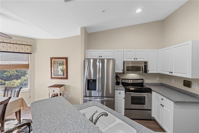 kitchen featuring lofted ceiling, stainless steel appliances, a sink, white cabinetry, and dark wood-style floors