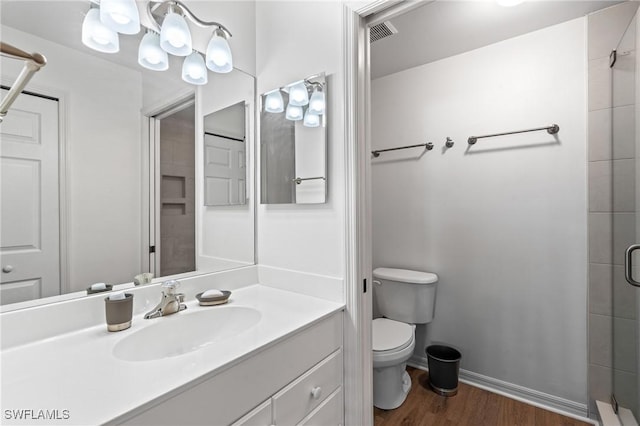 bathroom with toilet, wood finished floors, visible vents, baseboards, and tiled shower