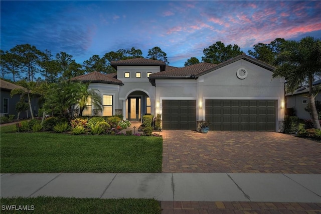 mediterranean / spanish home featuring a tiled roof, an attached garage, decorative driveway, a front lawn, and stucco siding