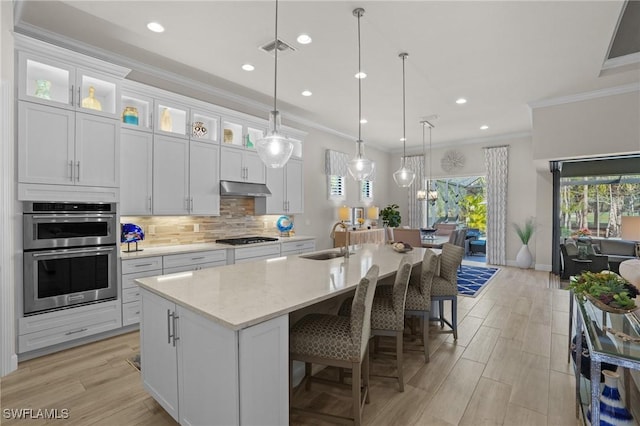 kitchen with gas stovetop, tasteful backsplash, stainless steel double oven, a sink, and under cabinet range hood