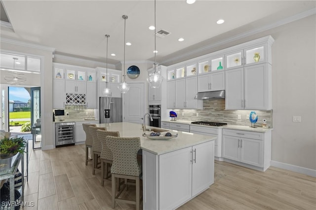 kitchen with under cabinet range hood, beverage cooler, white cabinetry, appliances with stainless steel finishes, and ornamental molding