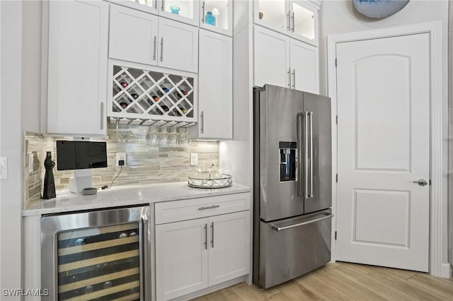 bar with wine cooler, tasteful backsplash, light wood-style floors, a bar, and stainless steel fridge