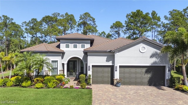 mediterranean / spanish house featuring decorative driveway, an attached garage, stucco siding, and a front yard