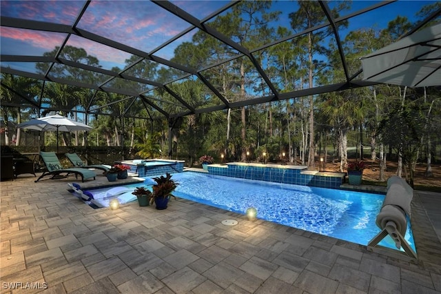 pool at dusk featuring a pool with connected hot tub, a patio area, and a lanai