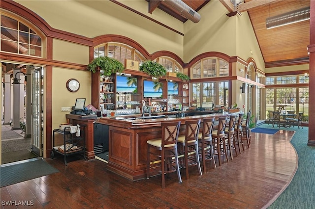 bar with a community bar, a towering ceiling, wooden ceiling, dark wood-style flooring, and beamed ceiling