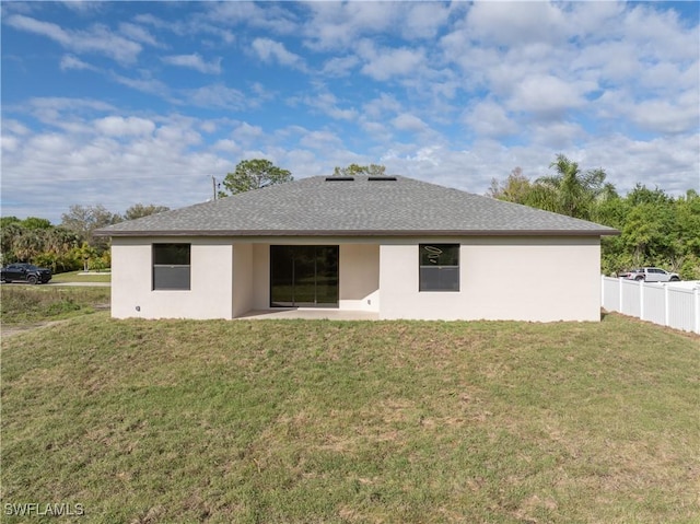 back of house with a shingled roof, a lawn, fence, and stucco siding