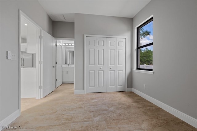 unfurnished bedroom featuring freestanding refrigerator, a closet, ensuite bath, and baseboards