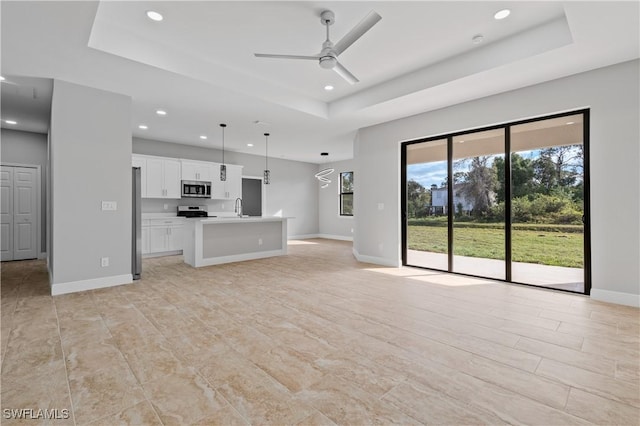 unfurnished living room with a tray ceiling, recessed lighting, a sink, ceiling fan, and baseboards