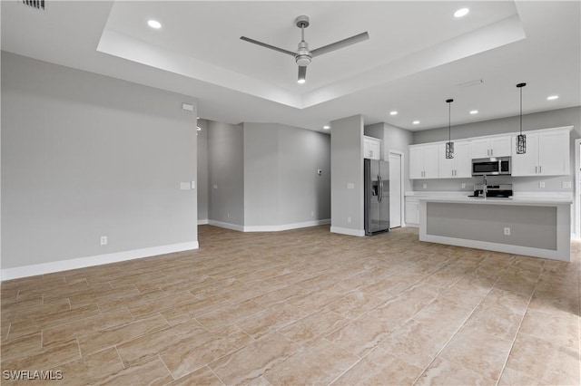 unfurnished living room featuring baseboards, ceiling fan, a tray ceiling, a sink, and recessed lighting