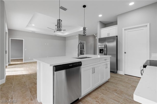 kitchen with stainless steel appliances, white cabinets, a raised ceiling, a center island with sink, and pendant lighting