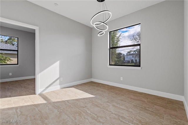 empty room with a notable chandelier, a wealth of natural light, and baseboards