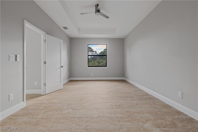 spare room with visible vents, a tray ceiling, a ceiling fan, and baseboards