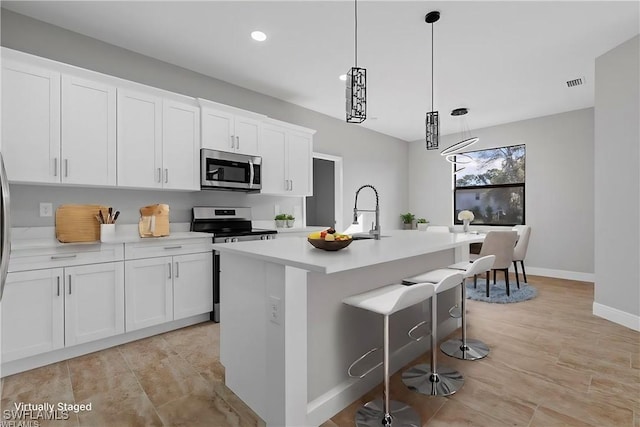 kitchen featuring a kitchen island with sink, white cabinets, light countertops, appliances with stainless steel finishes, and decorative light fixtures