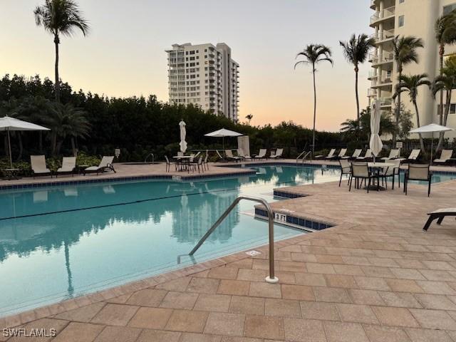 pool at dusk with a patio area and a community pool