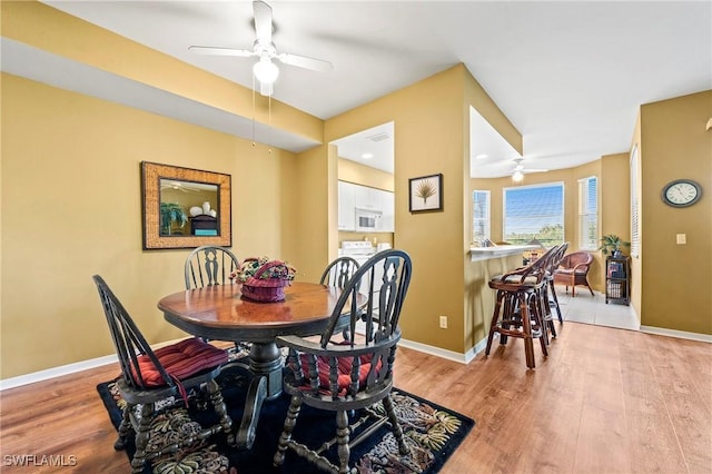 dining room featuring ceiling fan, light wood finished floors, and baseboards