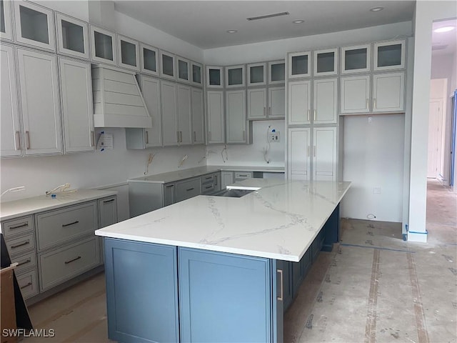 kitchen featuring light stone countertops, a spacious island, custom range hood, and glass insert cabinets