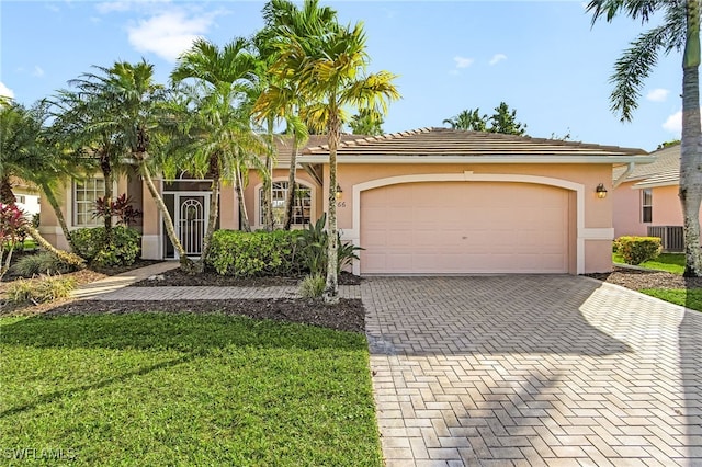 ranch-style house with an attached garage, cooling unit, decorative driveway, stucco siding, and a front yard