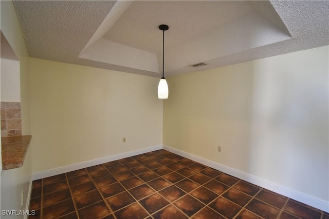 unfurnished dining area featuring a textured ceiling, a tray ceiling, visible vents, and baseboards