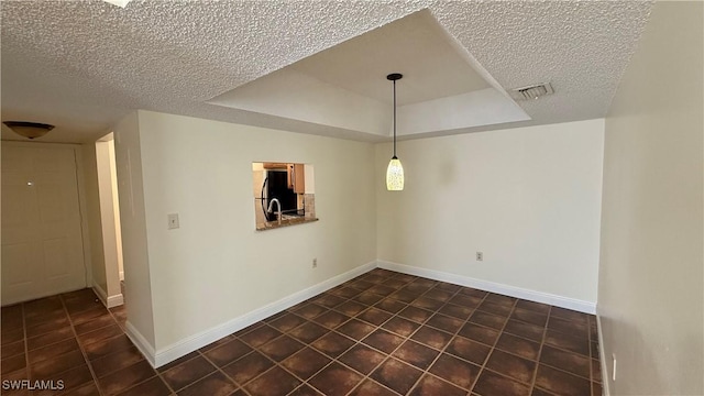 empty room with a textured ceiling, a tray ceiling, visible vents, and baseboards