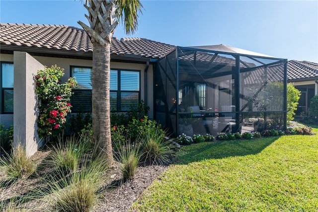 exterior space with a yard, a tiled roof, glass enclosure, and stucco siding