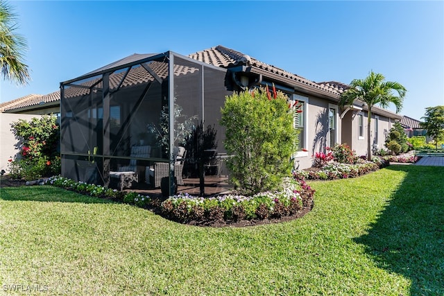 rear view of house with a yard, stucco siding, a tile roof, and a lanai