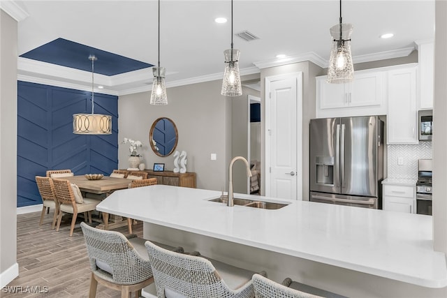 kitchen featuring tasteful backsplash, appliances with stainless steel finishes, light wood-type flooring, white cabinetry, and a sink