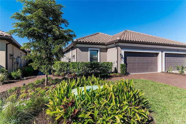 mediterranean / spanish-style house with a garage, driveway, a tile roof, and stucco siding