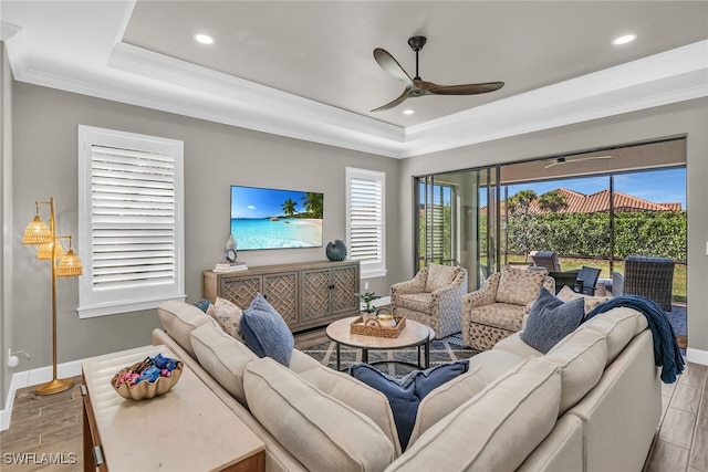 living area featuring ornamental molding, a tray ceiling, a ceiling fan, and baseboards