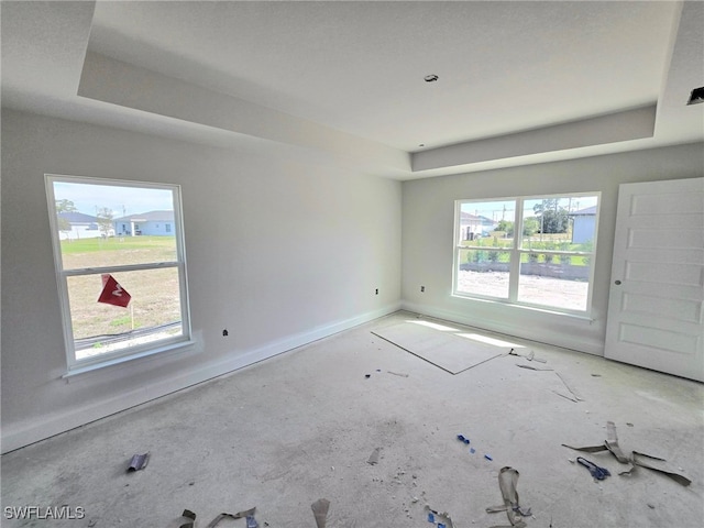 empty room with a tray ceiling, plenty of natural light, and baseboards