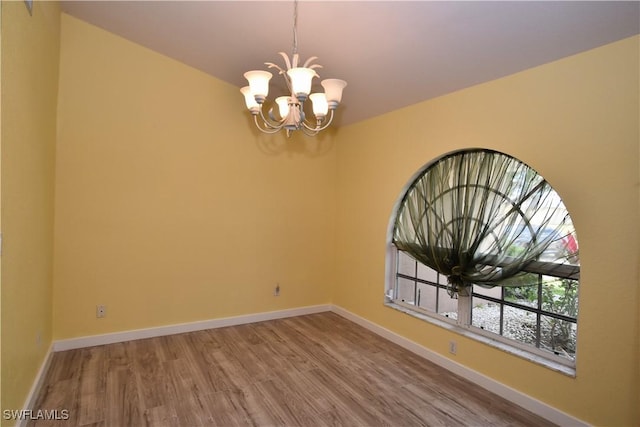 empty room with a notable chandelier, baseboards, and wood finished floors