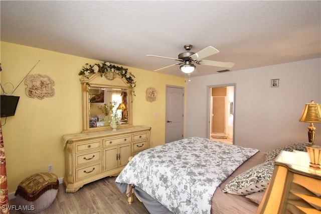 bedroom featuring light wood-type flooring, ensuite bath, visible vents, and a ceiling fan