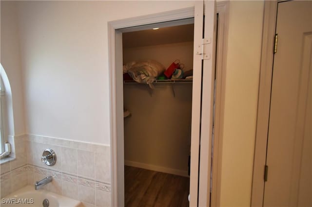 bathroom with a garden tub, baseboards, a walk in closet, and wood finished floors