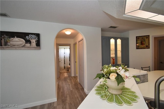 dining room with arched walkways, visible vents, baseboards, and wood finished floors