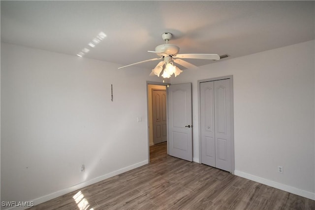 unfurnished bedroom featuring wood finished floors, visible vents, a ceiling fan, baseboards, and a closet