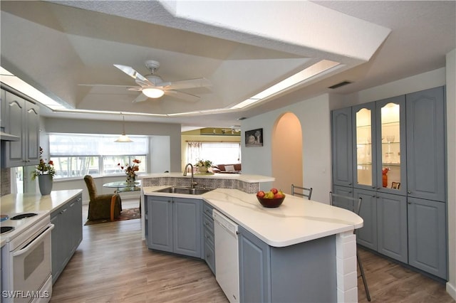 kitchen with a raised ceiling, visible vents, gray cabinetry, a sink, and white appliances