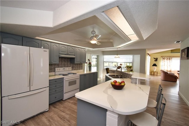 kitchen featuring a sink, a raised ceiling, white appliances, and gray cabinets