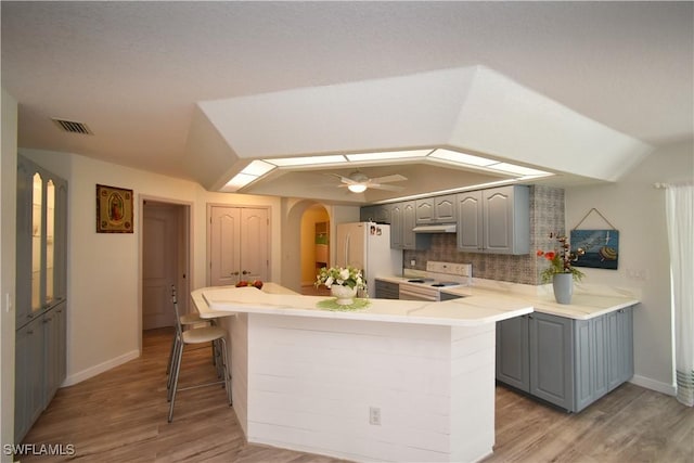 kitchen with white appliances, vaulted ceiling, under cabinet range hood, and gray cabinets