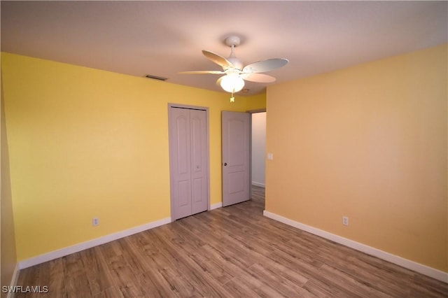 unfurnished bedroom with a closet, visible vents, ceiling fan, wood finished floors, and baseboards