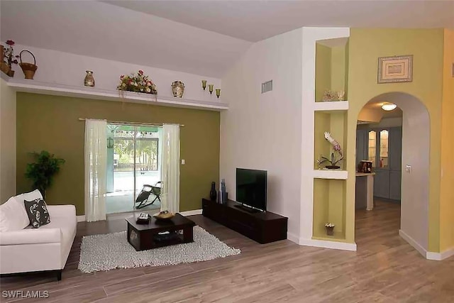 living area with arched walkways, visible vents, baseboards, and wood finished floors