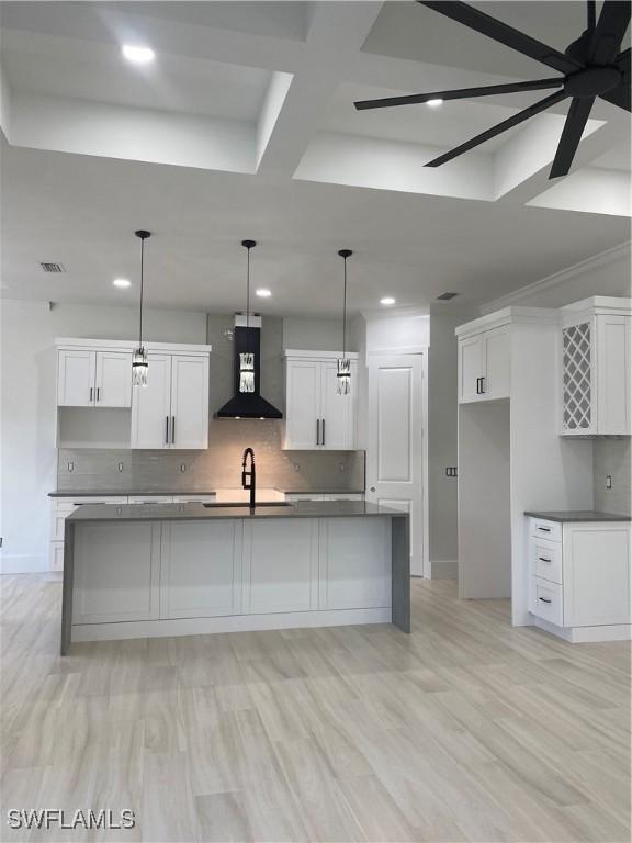 kitchen with wall chimney range hood, white cabinets, and a sink