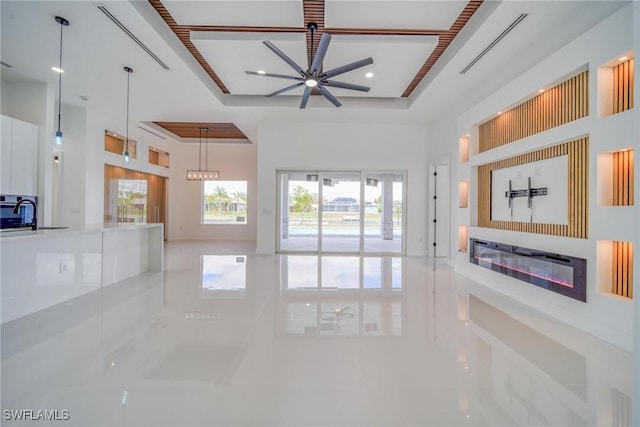 unfurnished living room with a raised ceiling, a glass covered fireplace, a towering ceiling, ceiling fan, and marble finish floor