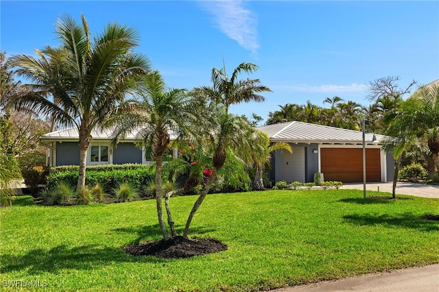 view of front facade with a garage, metal roof, driveway, and a front lawn