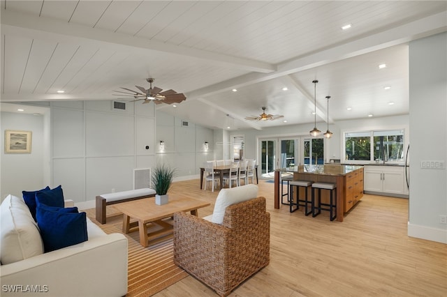 living area with visible vents, lofted ceiling with beams, light wood-style floors, a ceiling fan, and baseboards