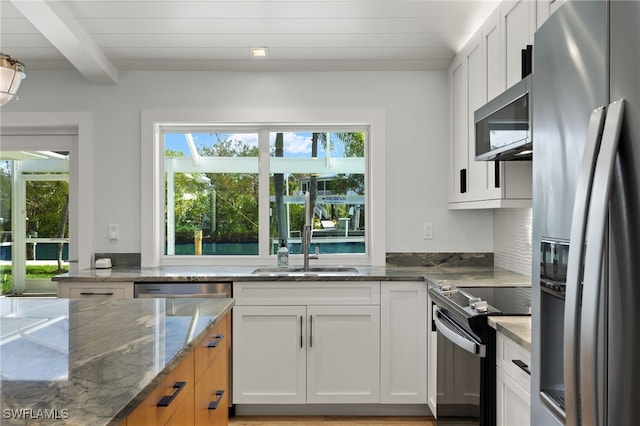 kitchen featuring stainless steel appliances, beamed ceiling, stone countertops, and white cabinets