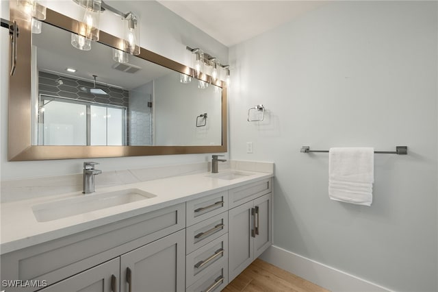 full bathroom featuring double vanity, a shower stall, baseboards, and a sink