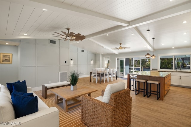 living area featuring vaulted ceiling with beams, visible vents, a decorative wall, and a ceiling fan