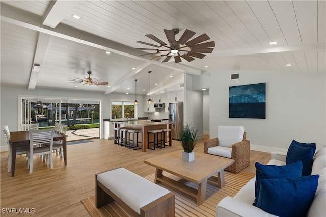 living room featuring lofted ceiling with beams, light wood-style flooring, visible vents, and baseboards