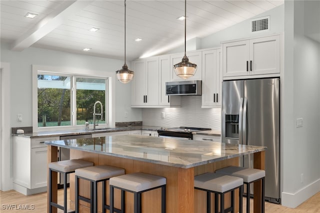 kitchen featuring a breakfast bar area, appliances with stainless steel finishes, vaulted ceiling with beams, a sink, and backsplash