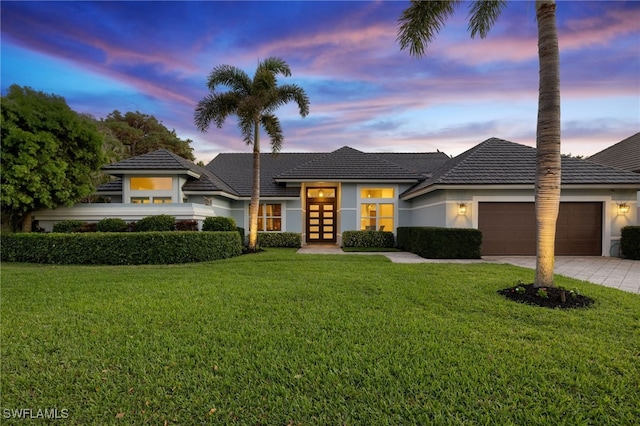 prairie-style home with an attached garage, driveway, french doors, stucco siding, and a front yard