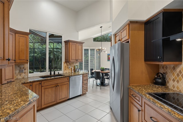 kitchen with pendant lighting, brown cabinets, appliances with stainless steel finishes, a sink, and dark stone counters